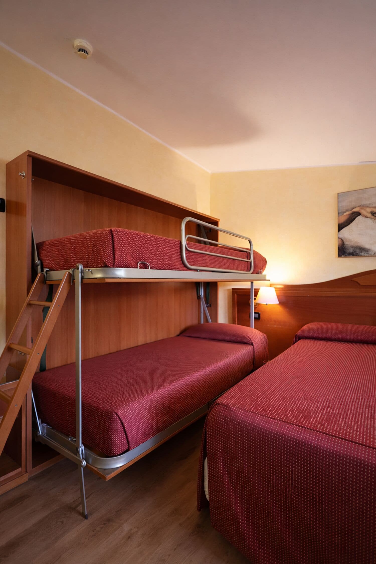 Habitación con literas, una escalera de madera, un escritorio y una lámpara.