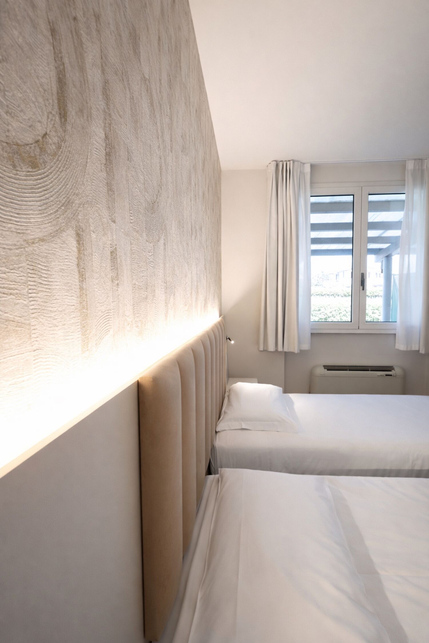 Une chambre d’hôtel avec un grand lit, une tête de lit, une fenêtre avec des rideaux et un radiateur.