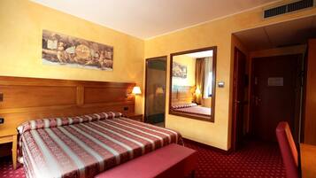 A hotel room with a large bed, a bedside table, a mirror, a bench, and a painting on the wall.
