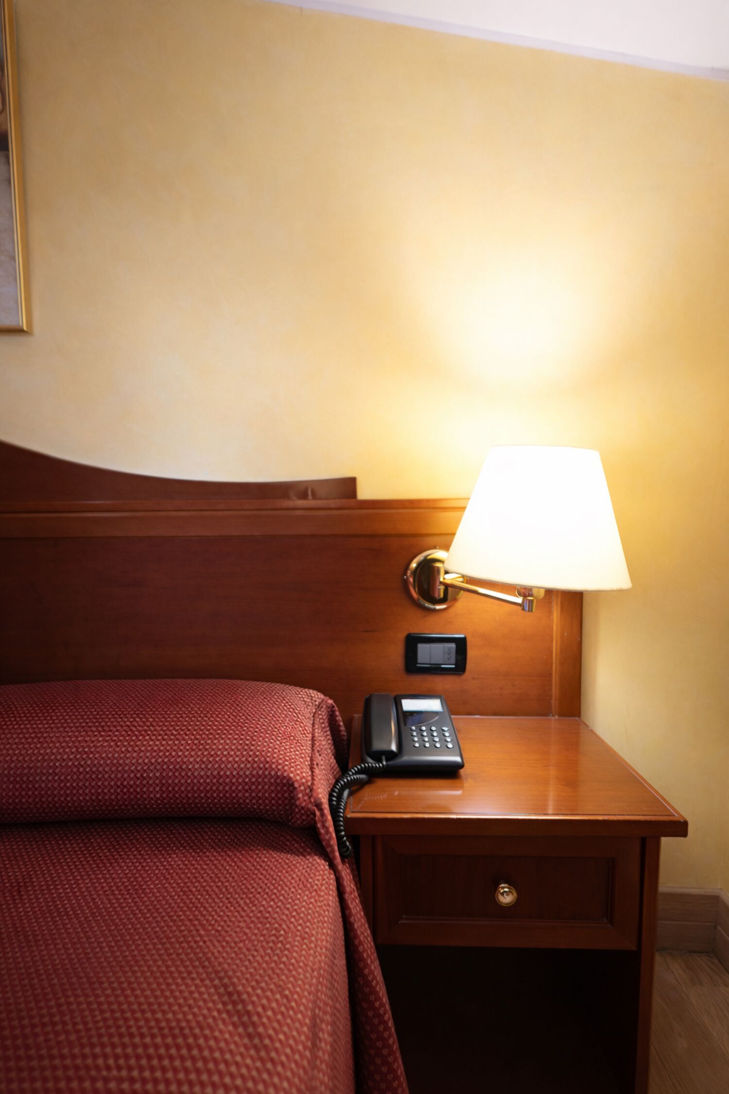 Habitació d'hotel amb llit, una taula de nit amb làmpada i un telèfon.
