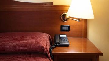 Een hotelkamer met een bed, nachtkastje met lamp en telefoon.