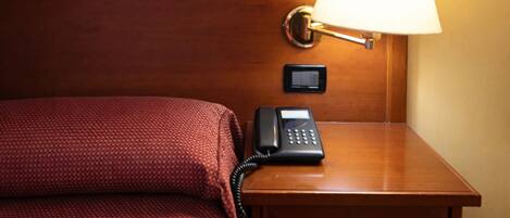 Habitació d'hotel amb llit, una taula de nit amb làmpada i un telèfon.