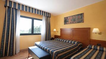 A hotel room with a large bed, a bench, two bedside tables, a painting on the wall, and curtains.