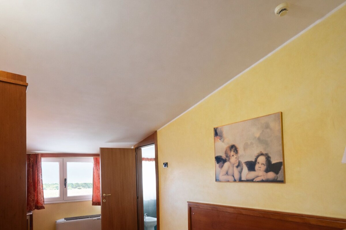 Ett hotellrum med en säng, ett fönster, ett badrum och en tavla på väggen.