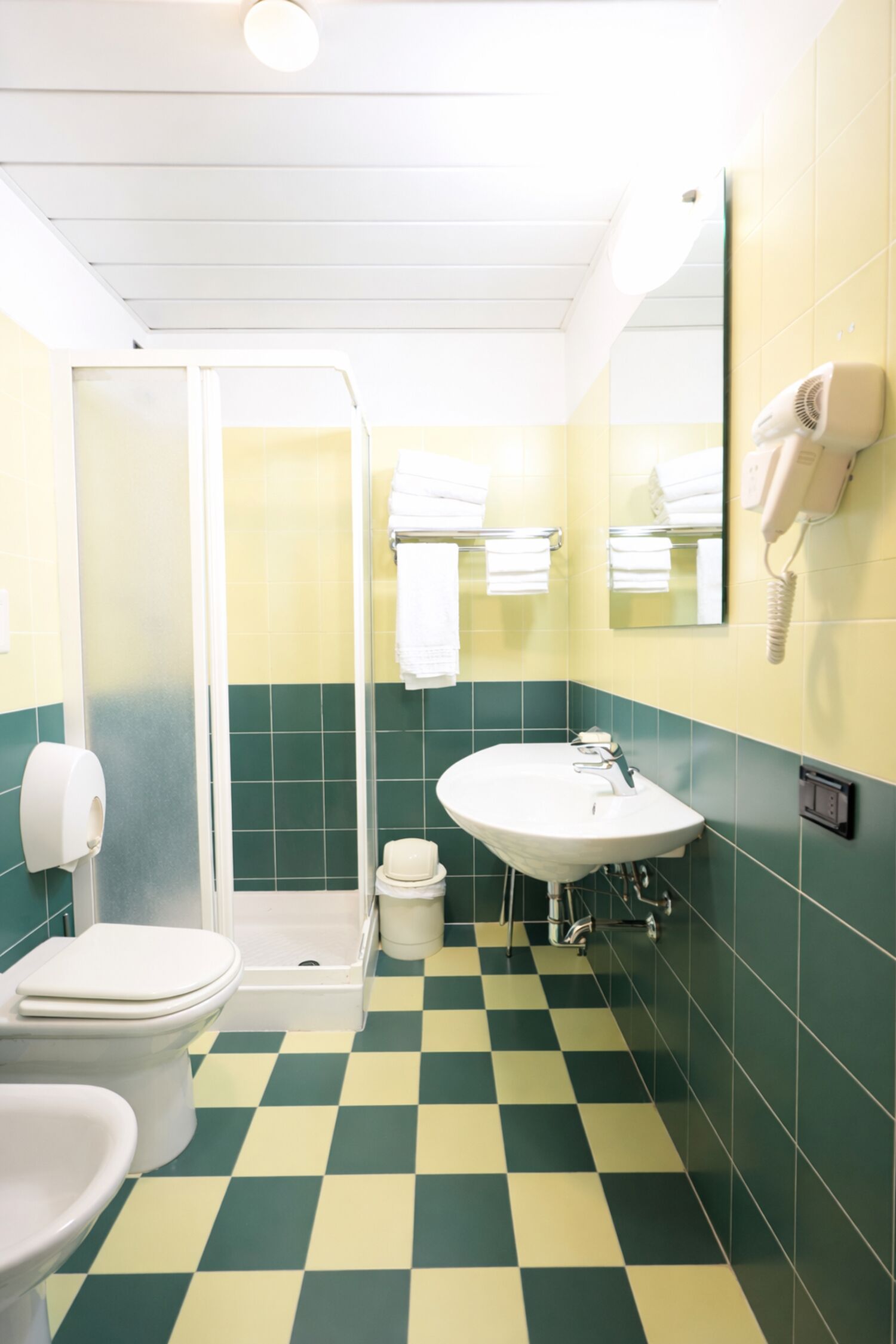 Kylpyhuone, jossa on ruutukuviollinen lattia, wc-istuin, pesuallas ja suihku.