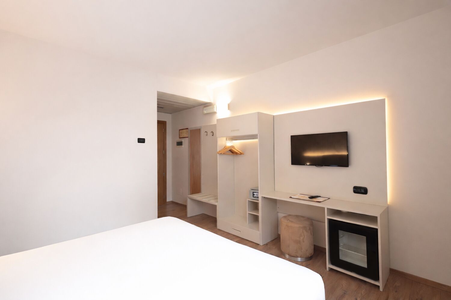 Una habitación de hotel moderna con una cama grande, un televisor de pantalla plana montado en la pared, una pequeña zona de estar y un mueble empotrado para la televisión.