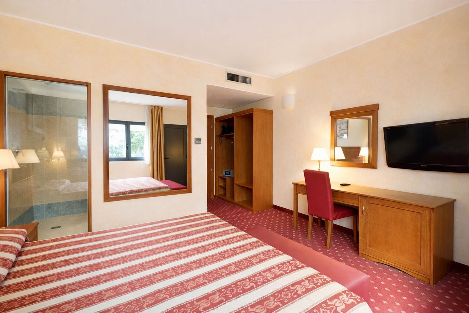 Ein Hotelzimmer mit Bett, Schreibtisch, Stuhl, Fernseher und Kleiderschrank.