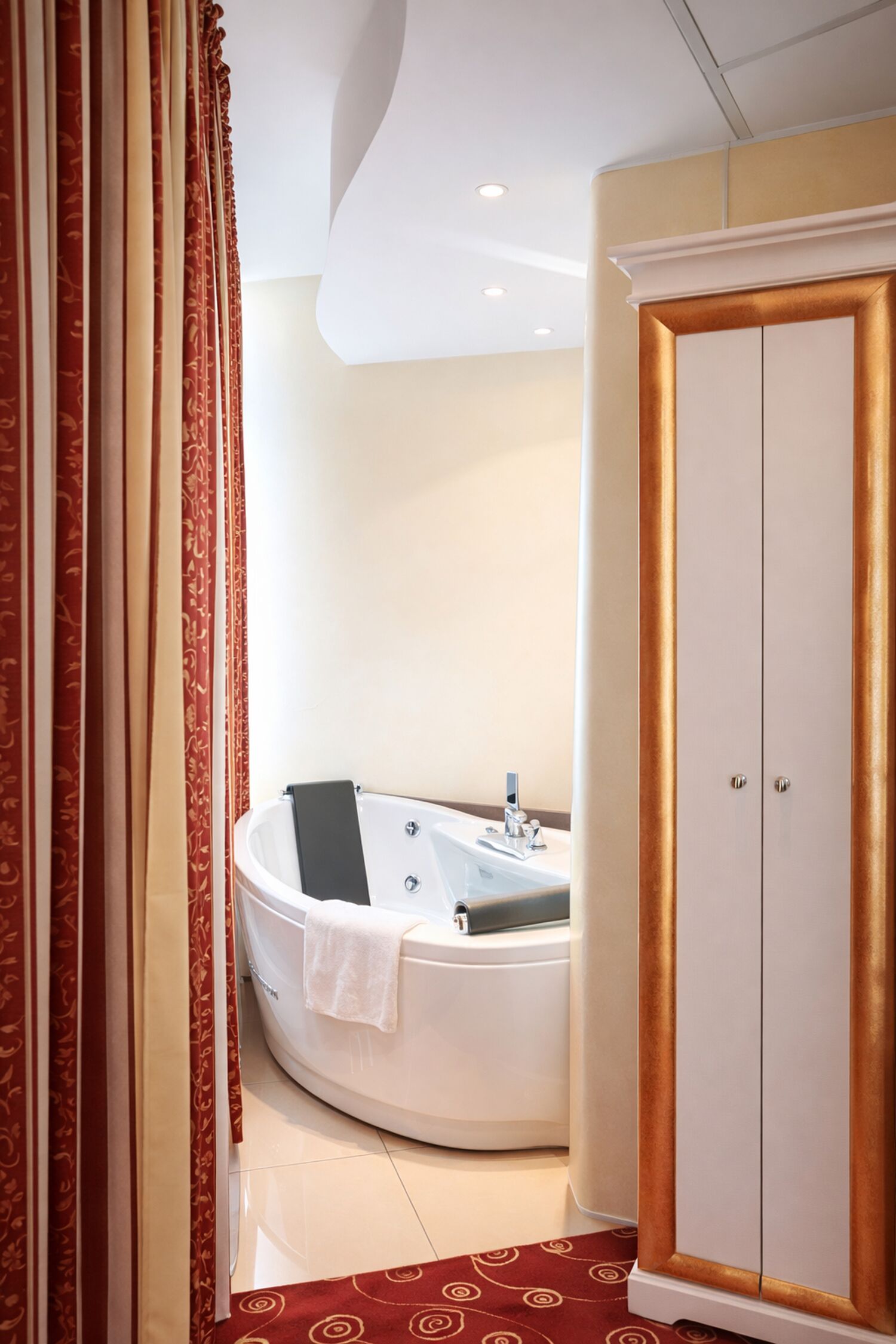 Ein modernes Badezimmer mit einer freistehenden Badewanne, einem weißen Schrank mit goldener Verzierung und einem roten Teppich mit Muster.