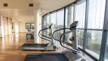 A gym with treadmills and exercise bikes, large windows, and wooden flooring.