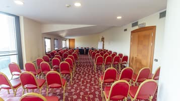 Un salón de conferencias con filas de sillas rojas, piso alfombrado y una gran puerta de madera.