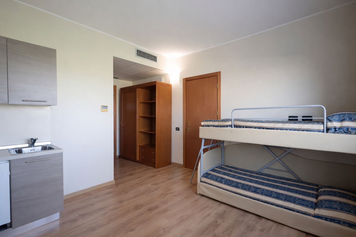 Een kleine kamer met een stapelbed, een kitchenette en een kledingkast.