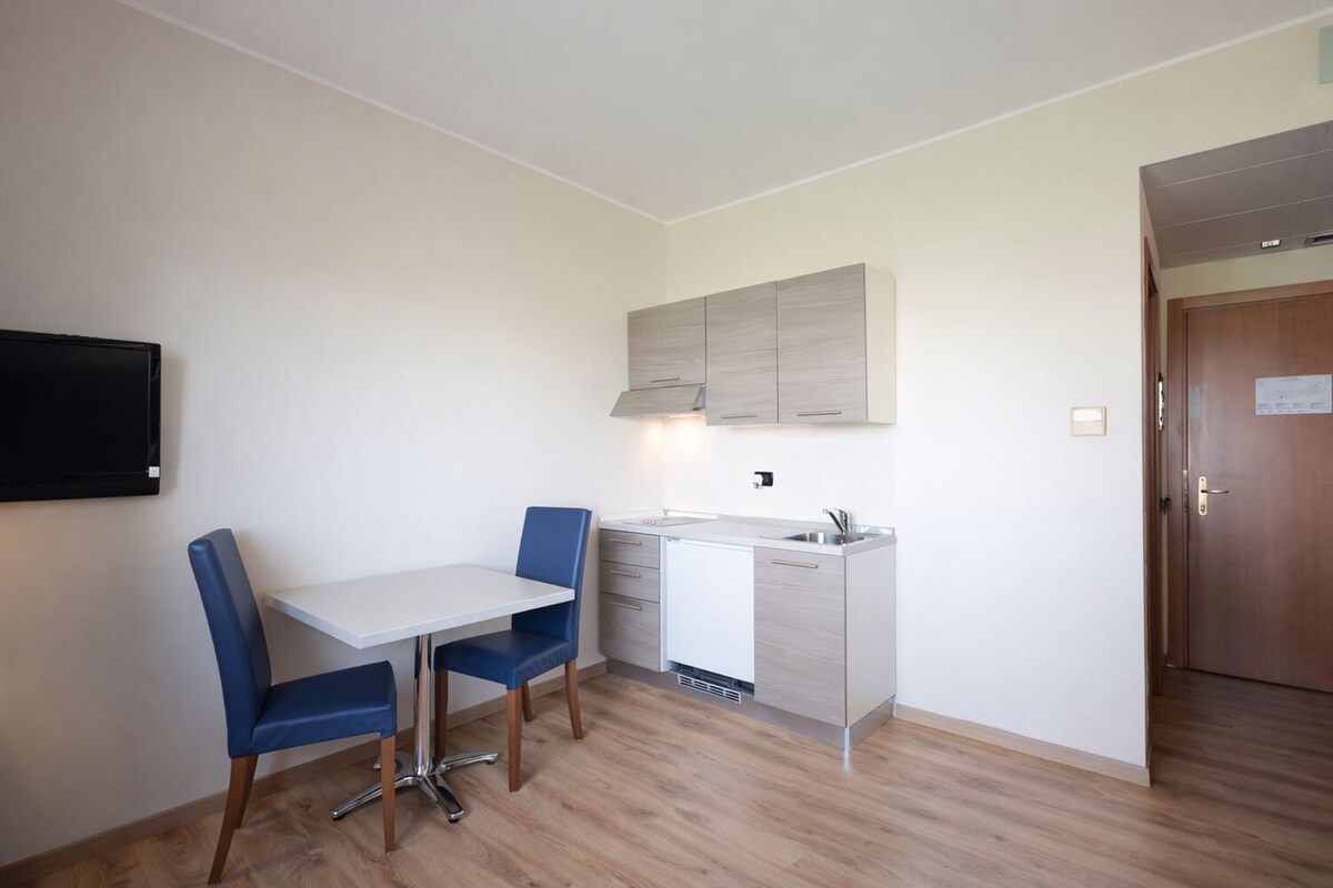 Ett kompakt kök med ett matbord och stolar, en inbyggd ugn och ett litet fönster.