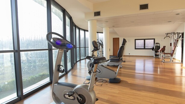 A gym with cardio machines, large windows, and wooden flooring. - LVG Hotel Collection – Riz (San Genesio ed Uniti)