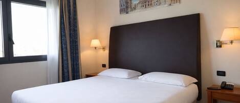 Habitación de hotel con una cama grande, una mesita de noche, una lámpara y un cuadro en la pared.