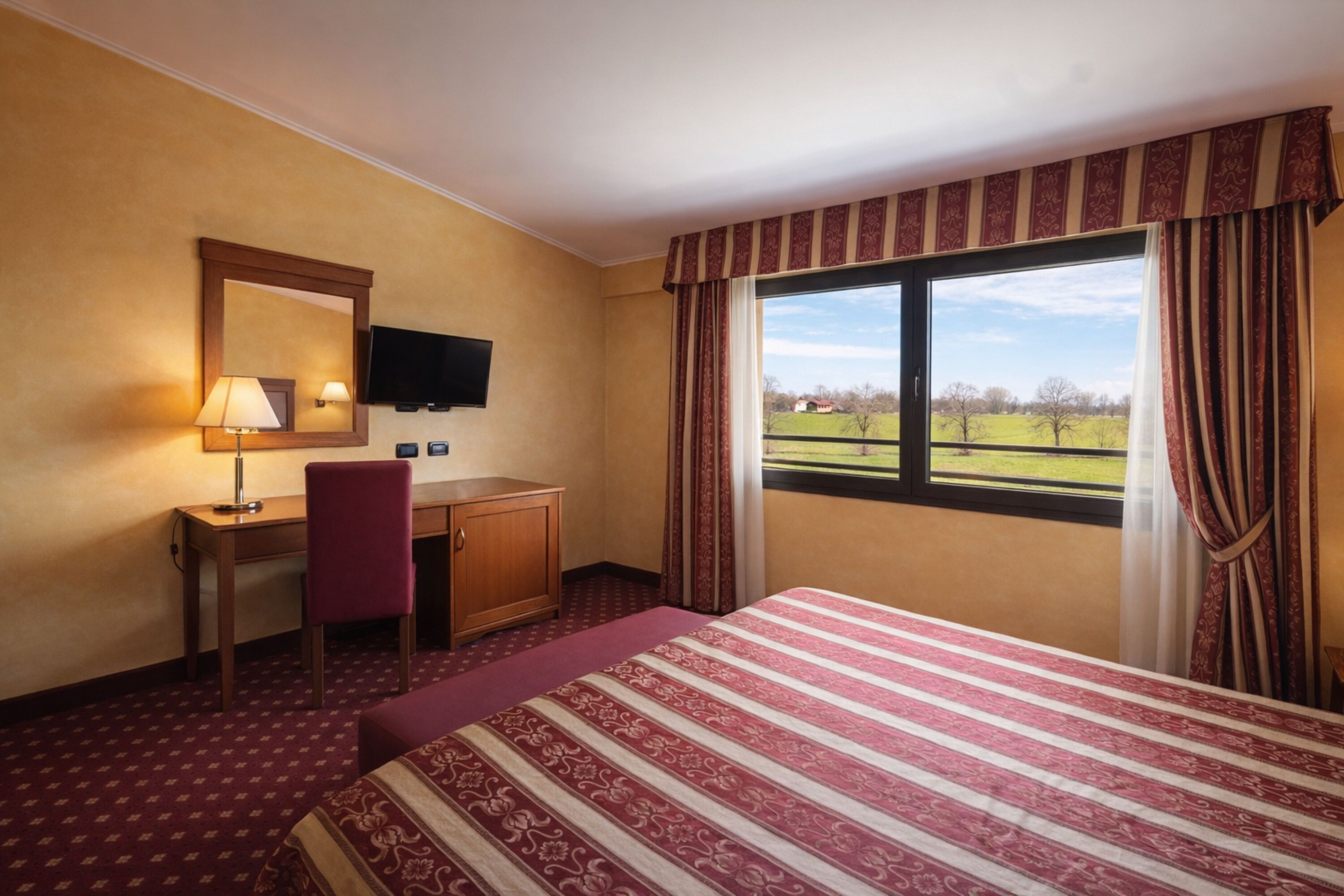 A hotel room with a bed, a desk, a chair, a television, and a window with curtains.