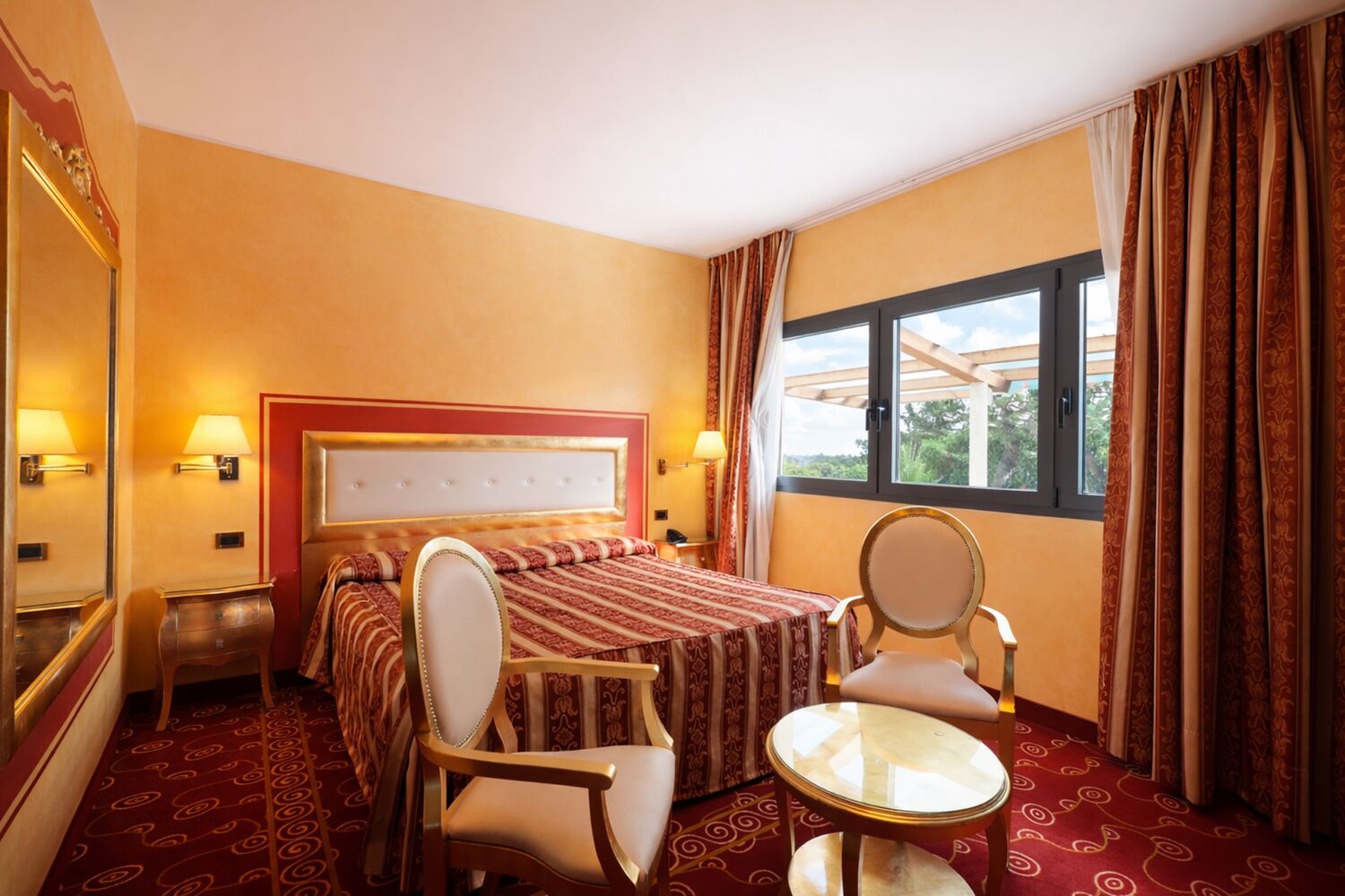 Habitación de hotel con cama, dos sillas, una mesita y una ventana con cortinas.