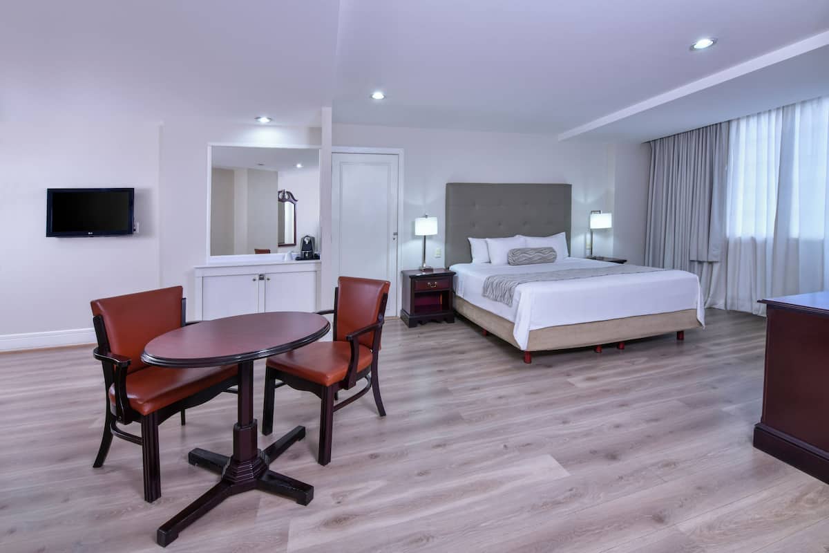 Ein Hotelzimmer mit Bett, Nachttischen, einem Schreibtisch mit Stühlen, einem Fernseher und einem Spiegel.