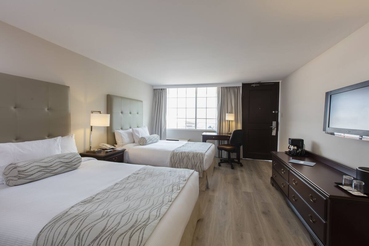 Ein Hotelzimmer mit zwei Betten, einem Schreibtisch, einem Stuhl, einer Kommode und einem an der Wand befestigten Fernseher.