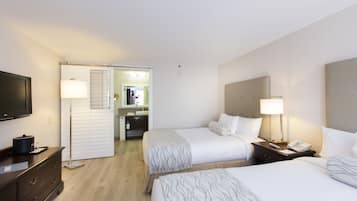 Ein Hotelzimmer mit zwei Betten, einem Fernseher, einem Schreibtisch und einem durch eine offene Tür einsehbaren Badezimmer.