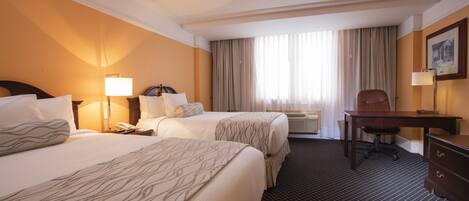 A hotel room with two beds, a desk, a chair, a telephone, and a window with curtains.