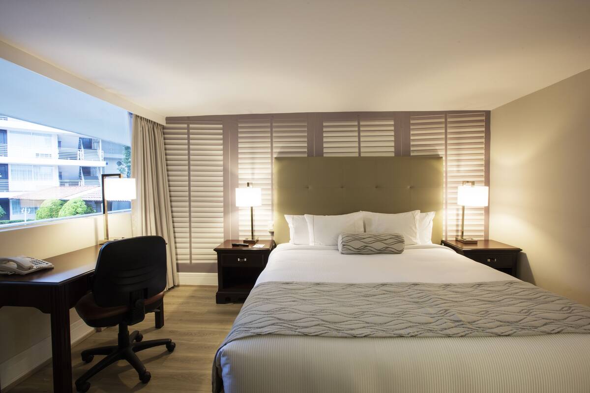 Ein Hotelzimmer mit Bett, Schreibtisch, Stuhl und einem Fenster mit Jalousien.