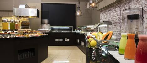 Zona de bufé con diversos alimentos y bebidas, un mostrador negro y una pared de ladrillo.