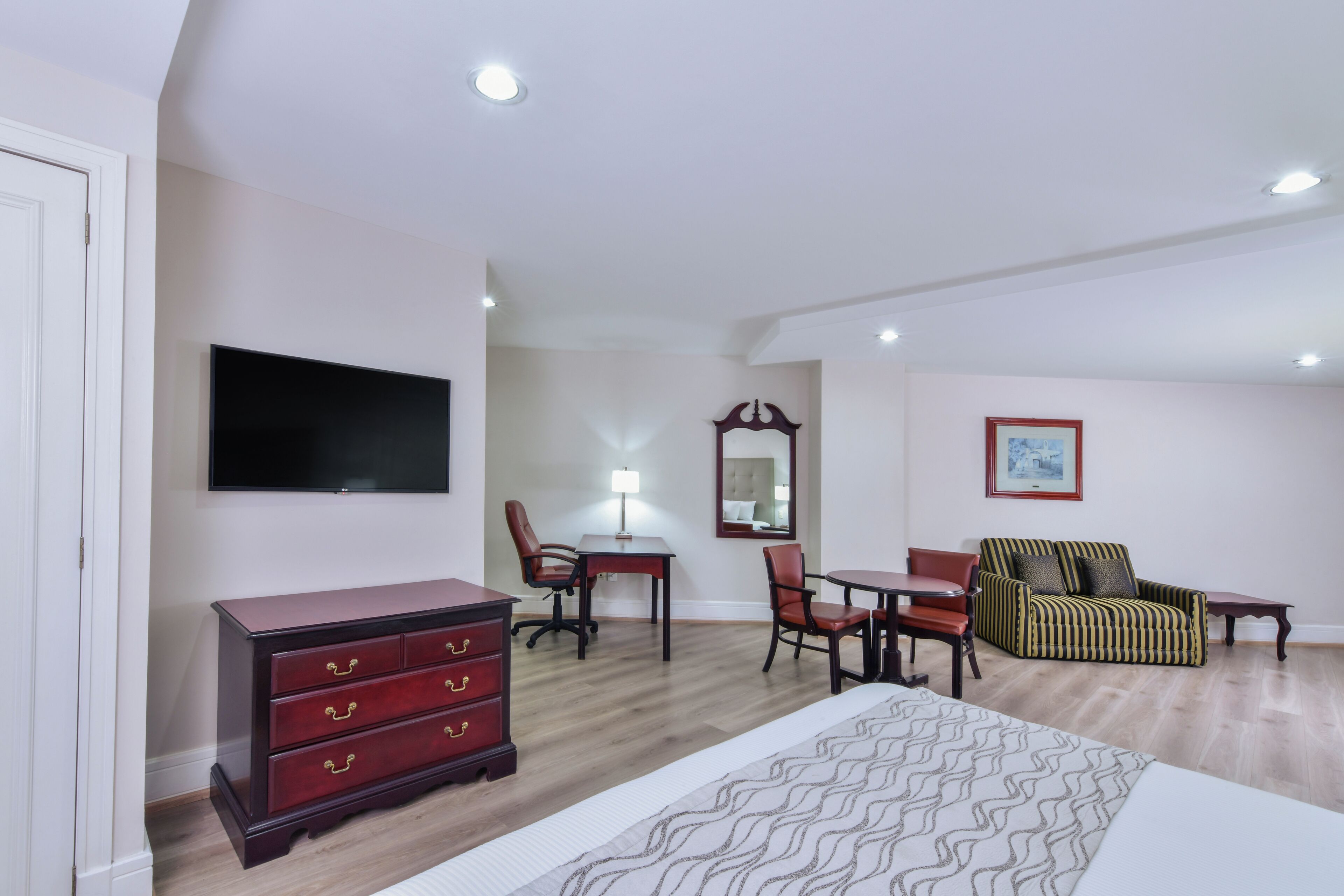 Une chambre d’hôtel comprenant un lit, une commode, un bureau avec une chaise, un canapé, un téléviseur fixé au mur et un tableau encadré accroché au mur.