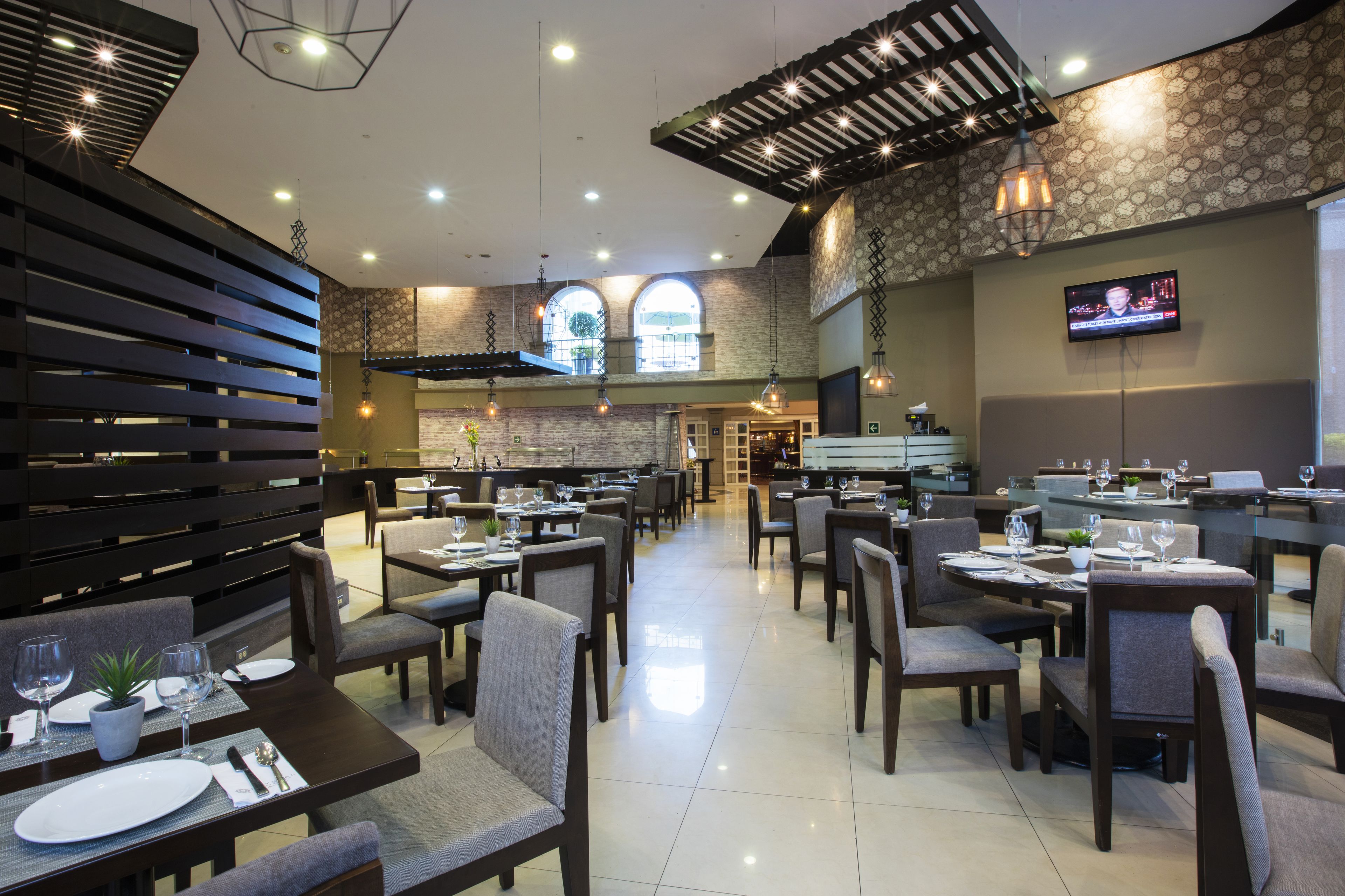 A spacious restaurant with multiple dining tables and chairs, a television screen on the wall, and a modern interior design.