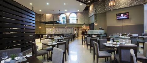A spacious restaurant with multiple dining tables and chairs, a television screen on the wall, and a modern interior design.