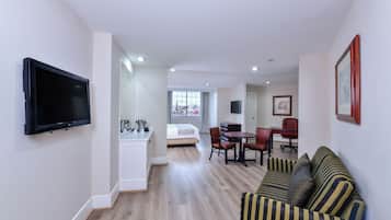 A modern hotel room with a flat-screen TV, a dining area with a table and chairs, a sofa, and a bed.