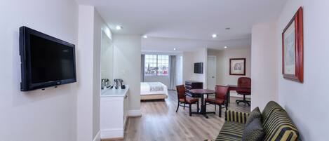 A modern hotel room with a flat-screen TV, a dining area with a table and chairs, a sofa, and a bed.
