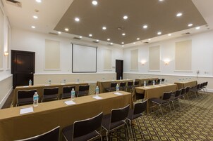 Un salón de conferencias con varias mesas y sillas, equipado con botellas de agua y tarjetas de identificación.