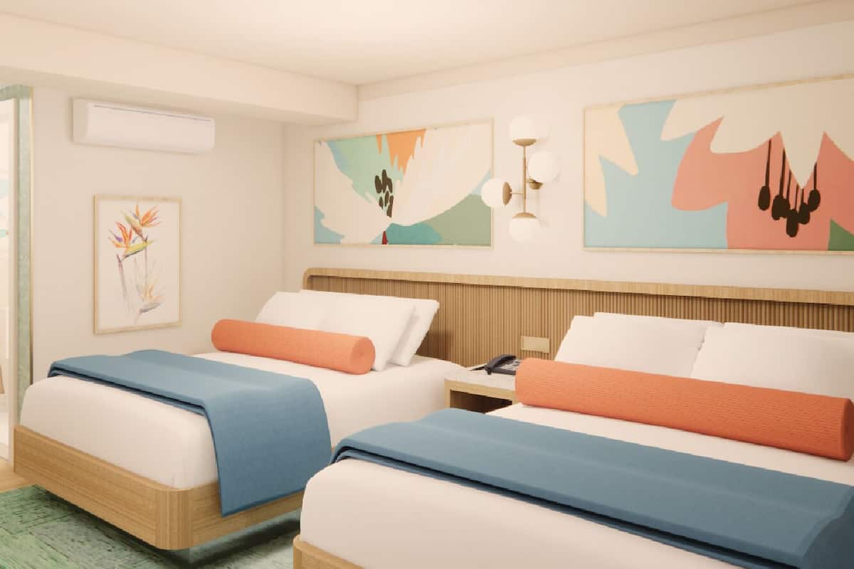 A hotel room with two beds, each with a blue and orange bedspread, a wooden headboard, and a wall-mounted air conditioning unit.