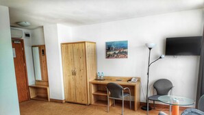 A room with a wooden desk, two chairs, a small table, a TV, and a wardrobe. - Logos (Warsaw)