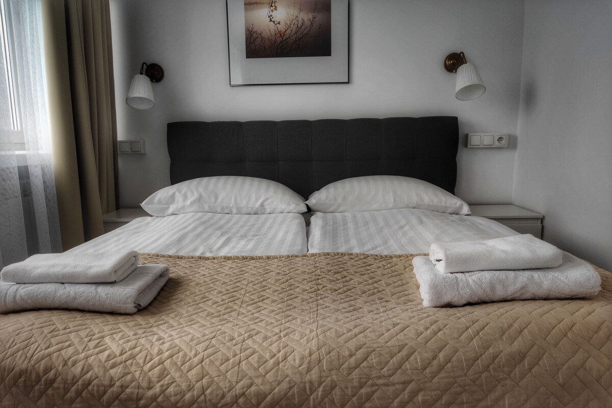 A neatly made double bed with a quilted bedspread, two white pillows, and folded towels on either side.