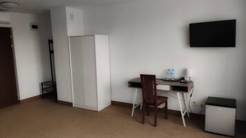 Una habitación con escritorio, silla, refrigerador pequeño y televisor en la pared.