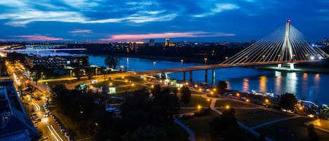 Un puente moderno con múltiples cables, un río y zona urbana circundante con calles y vegetación.