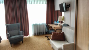 A hotel room with a sofa, armchair, desk, and a television. - Logos (Warsaw)