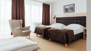 A hotel room with a large bed, two smaller beds, a chair, and a bedside table. - Logos (Warsaw)