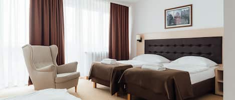 A hotel room with a large bed, two smaller beds, a chair, and a bedside table.