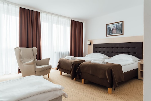 A hotel room with a large bed, two smaller beds, a chair, and a bedside table.