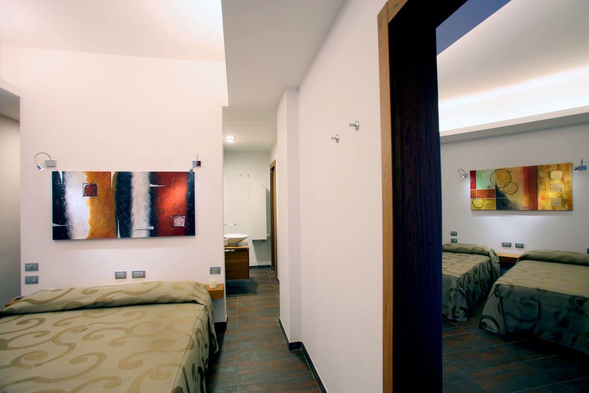A hotel room with two beds, a bathroom, and a hallway leading to another room.