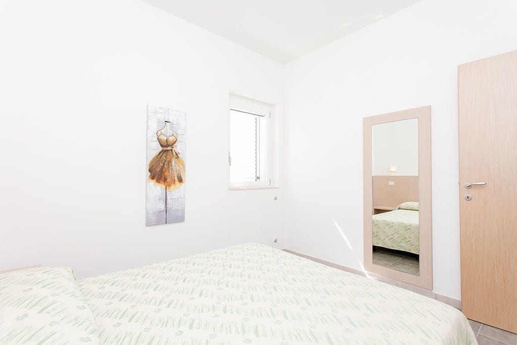 A bedroom with a bed, a window, a mirror, and a door.