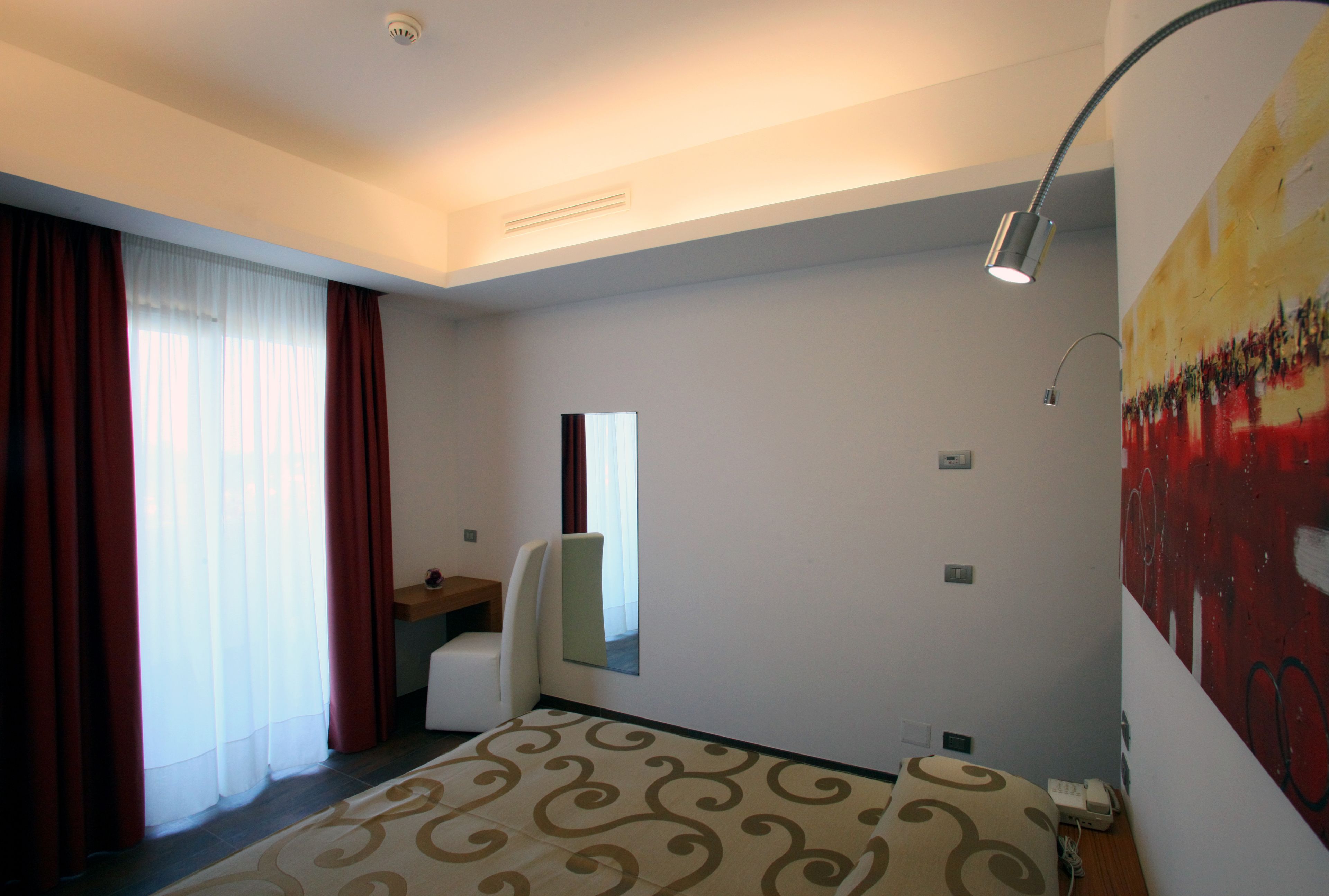 A modern hotel room with a large bed, a desk, a chair, and a painting on the wall.