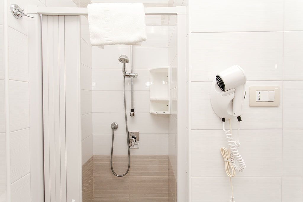 A shower area with a handheld hair dryer mounted on the wall, a towel hanging on a rack, and a small shelf.