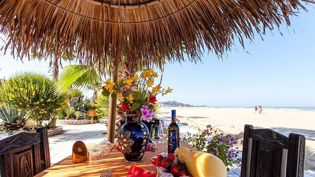 A table set for two with a view of the beach, a thatched roof, and a decorative vase with flowers. - Scialì Hotel (Vieste)