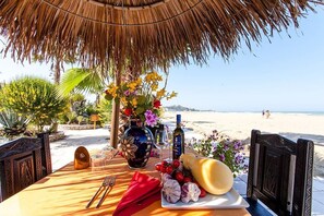 A table set for two with a view of the beach, a thatched roof, and a decorative vase with flowers. - Scialì Hotel (Vieste)