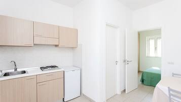 Eine kleine Küche mit Spüle, Herd und Kühlschrank, die in einen Essbereich mit Tisch und Stühlen übergeht.