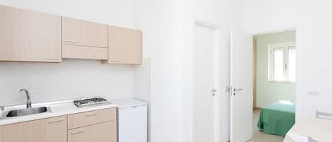 A compact kitchen with a sink, stove, and refrigerator, leading to a small dining area with a table and chairs.