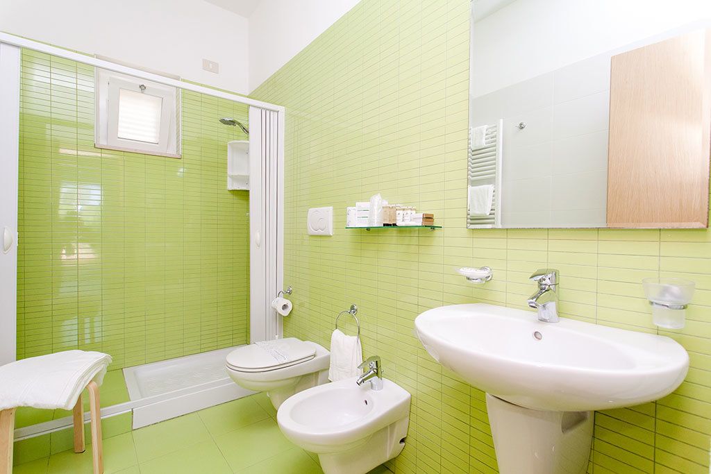 Un baño con baldosas verdes, ducha, inodoro, bidé y dos lavamanos.